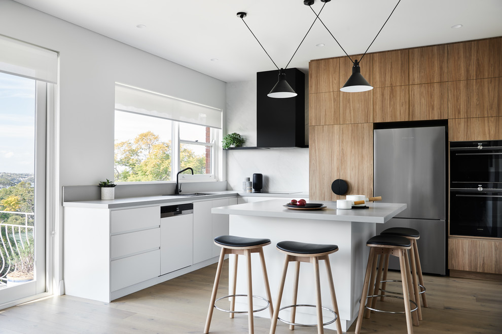 This is an example of a mid-sized contemporary l-shaped kitchen in Sydney with a double-bowl sink, flat-panel cabinets, medium wood cabinets, white splashback, stainless steel appliances, medium hardwood floors, with island, brown floor and grey benchtop.