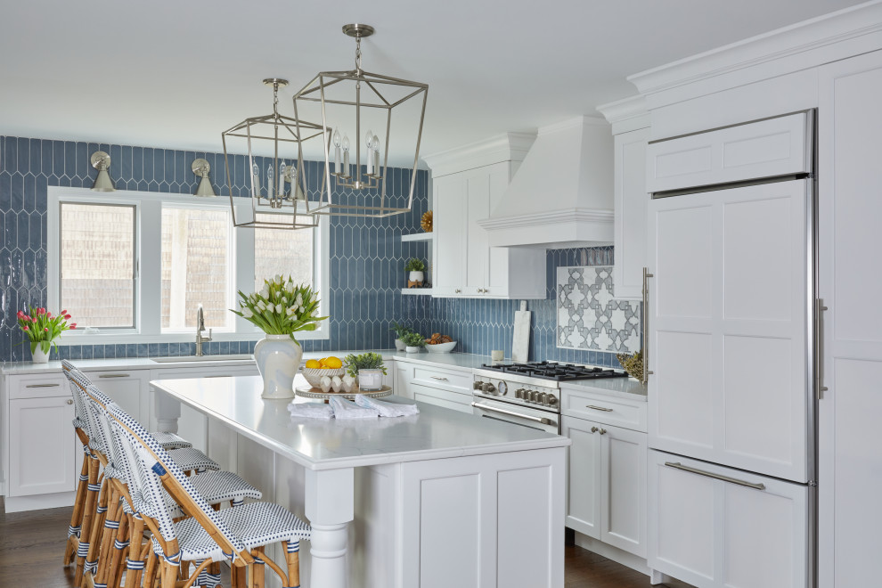 Example of a transitional dark wood floor and brown floor kitchen design with an undermount sink, recessed-panel cabinets, white cabinets, quartz countertops, blue backsplash, porcelain backsplash, paneled appliances, an island and white countertops