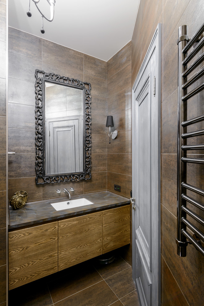 This is an example of a mid-sized traditional powder room in Novosibirsk with flat-panel cabinets, brown tile, porcelain tile, porcelain floors, an undermount sink, solid surface benchtops, medium wood cabinets and brown floor.