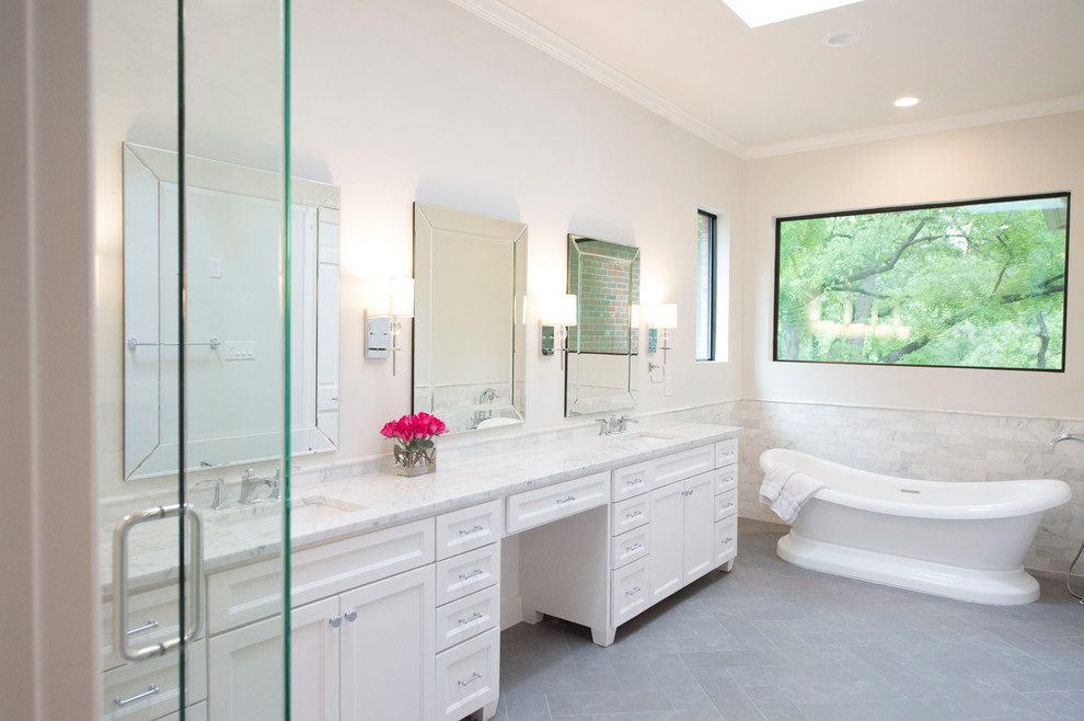 This is an example of a large transitional master bathroom in Dallas with white cabinets, a freestanding tub, a corner shower, gray tile, marble, white walls, porcelain floors, an undermount sink, marble benchtops, grey floor and a hinged shower door.
