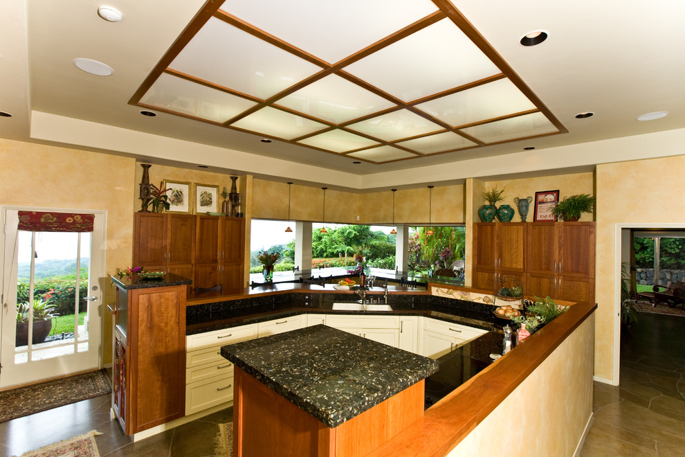 Large tropical u-shaped eat-in kitchen in Hawaii with a double-bowl sink, shaker cabinets, brown cabinets, granite benchtops, beige splashback, stone slab splashback, panelled appliances, concrete floors, multiple islands, brown floor and black benchtop.