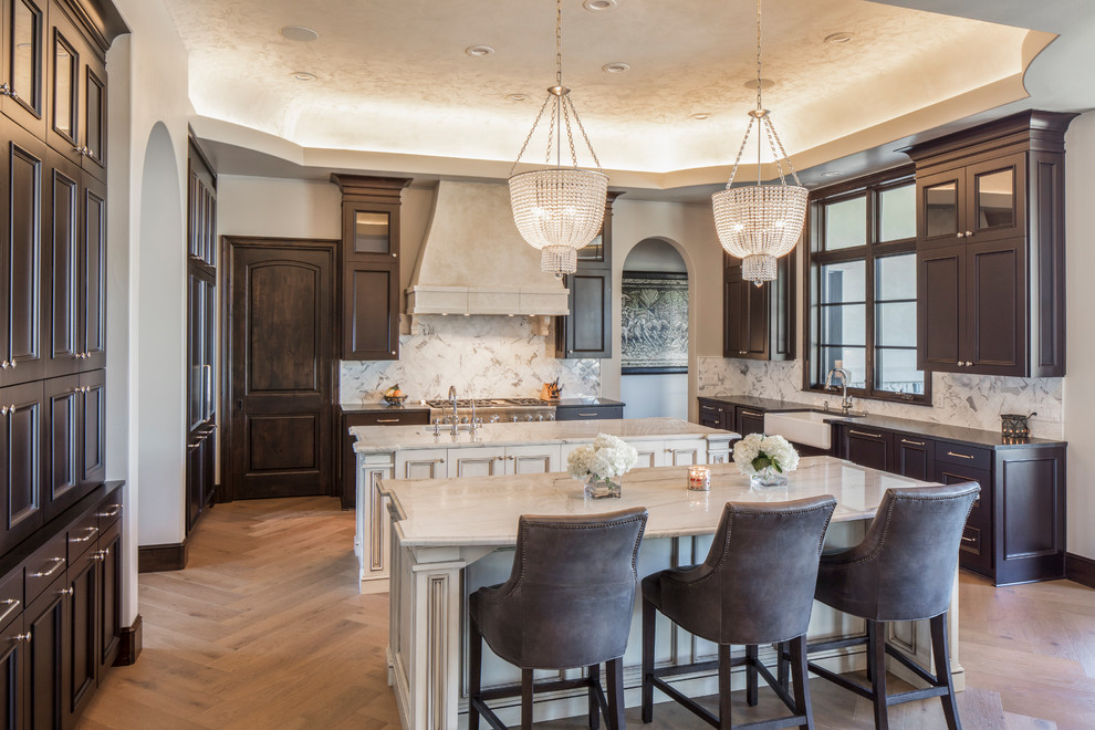 Inspiration for a large traditional u-shaped separate kitchen in Austin with a farmhouse sink, beaded inset cabinets, dark wood cabinets, marble benchtops, white splashback, marble splashback, panelled appliances, medium hardwood floors, multiple islands and brown floor.