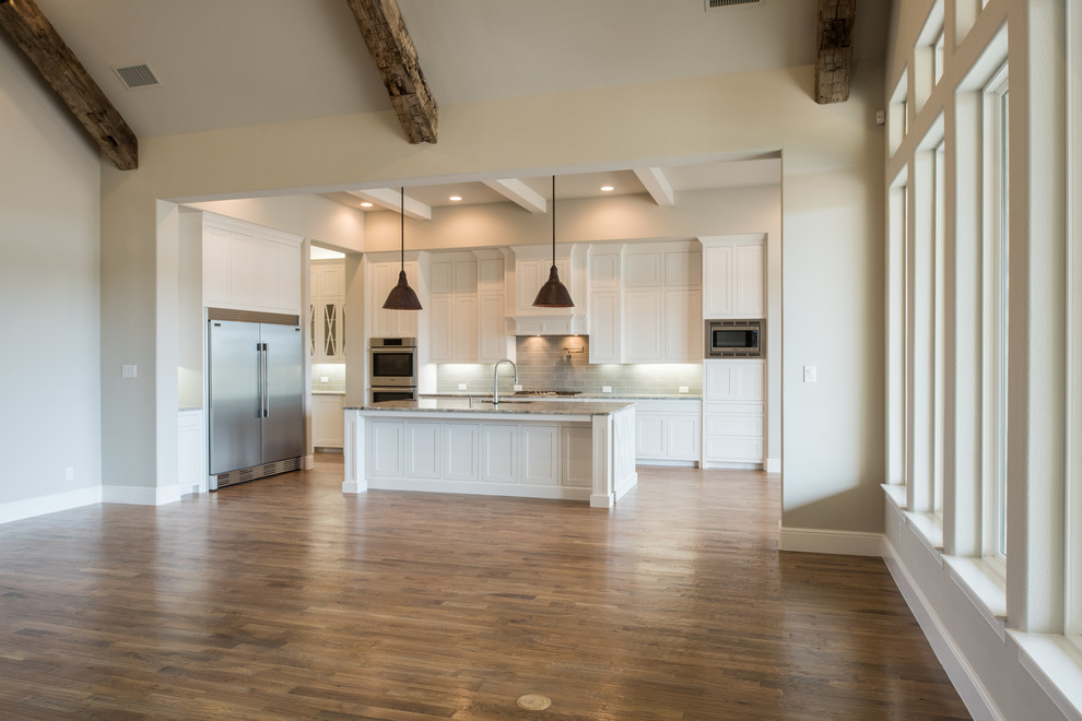 Large transitional u-shaped medium tone wood floor and brown floor eat-in kitchen photo in Dallas with a drop-in sink, recessed-panel cabinets, white cabinets, granite countertops, beige backsplash, ceramic backsplash, stainless steel appliances, an island and multicolored countertops