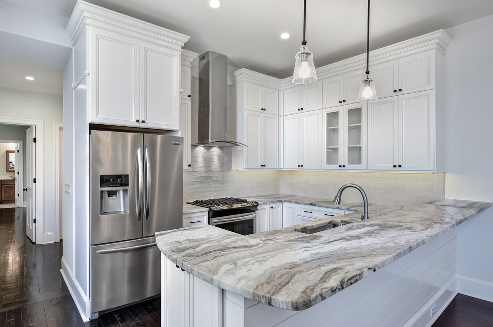 Small traditional kitchen in Charleston with a single-bowl sink, recessed-panel cabinets, white cabinets, granite benchtops, beige splashback, stone tile splashback, stainless steel appliances, dark hardwood floors, a peninsula and brown floor.