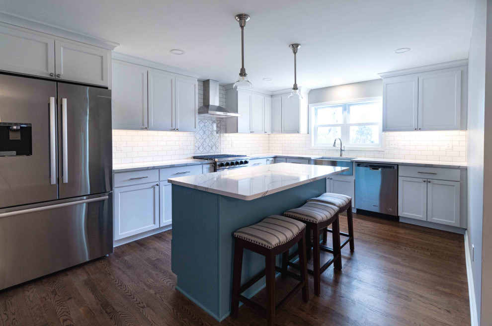 Inspiration for a large contemporary l-shaped eat-in kitchen in Cleveland with a farmhouse sink, shaker cabinets, blue cabinets, quartzite benchtops, white splashback, ceramic splashback, stainless steel appliances, medium hardwood floors, with island, brown floor and white benchtop.