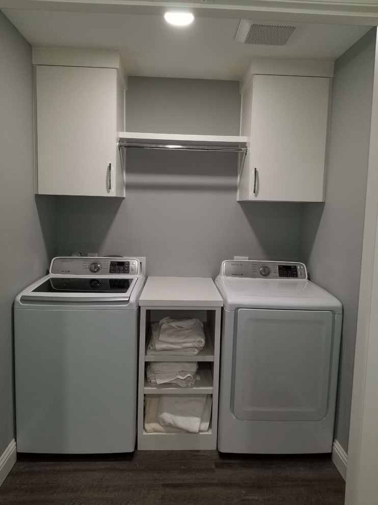 Photo of a small transitional single-wall dedicated laundry room in Dallas with flat-panel cabinets, white cabinets, laminate benchtops, grey walls, laminate floors, a side-by-side washer and dryer, brown floor and white benchtop.