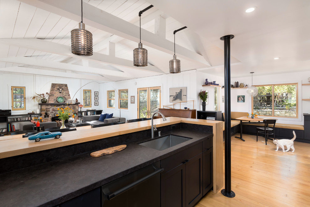 This is an example of a mid-sized country l-shaped open plan kitchen in Los Angeles with an undermount sink, shaker cabinets, black cabinets, granite benchtops, black splashback, stone slab splashback, black appliances, medium hardwood floors, a peninsula and orange floor.