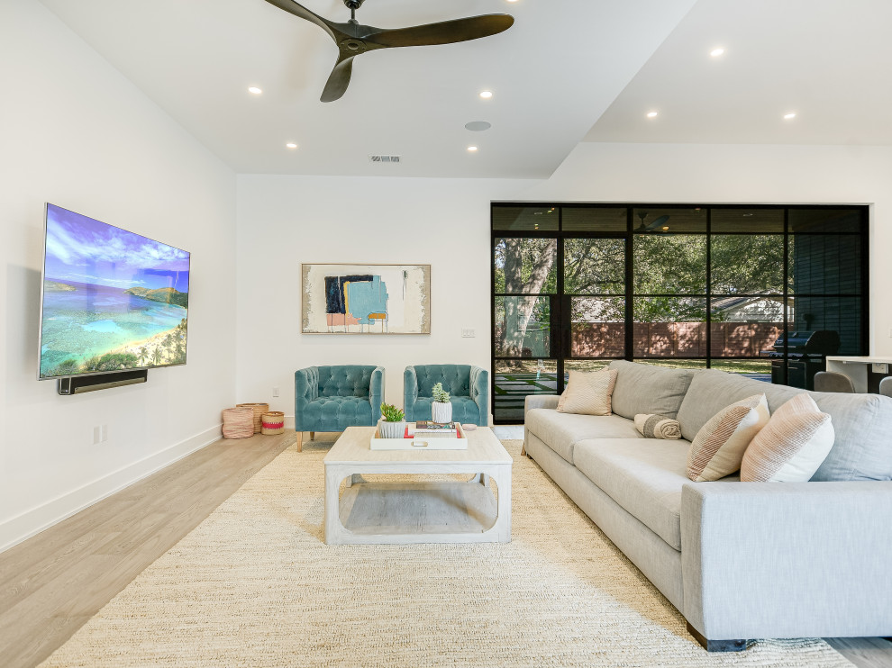 Photo of a mid-sized modern open concept family room in Austin with white walls, light hardwood floors and a wall-mounted tv.