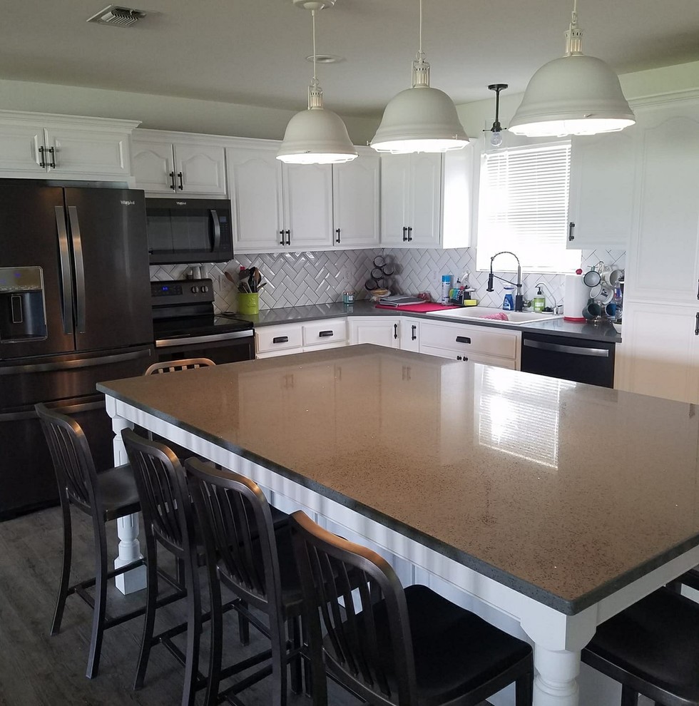 Example of a mid-sized transitional u-shaped dark wood floor and brown floor kitchen design with a drop-in sink, raised-panel cabinets, white cabinets, quartz countertops, white backsplash, ceramic backsplash, black appliances, an island and gray countertops