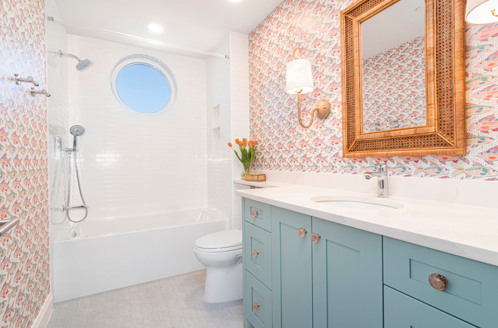 Photo of a medium sized nautical family bathroom in Miami with shaker cabinets, turquoise cabinets, a built-in bath, a shower/bath combination, a one-piece toilet, white tiles, metro tiles, multi-coloured walls, porcelain flooring, a submerged sink, engineered stone worktops, beige floors, a shower curtain, white worktops, a wall niche, a single sink, a built in vanity unit and wallpapered walls.
