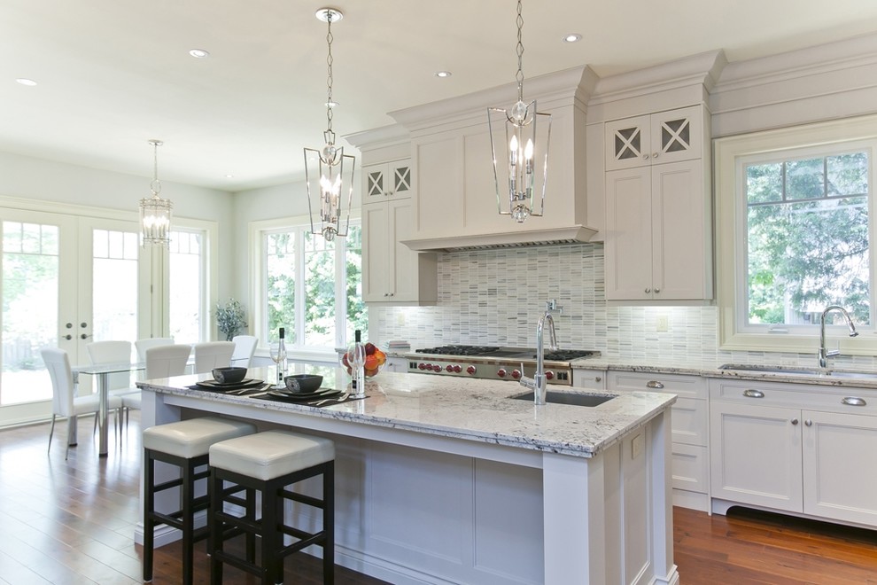 Eat-in kitchen - large transitional galley medium tone wood floor and brown floor eat-in kitchen idea in Toronto with an undermount sink, shaker cabinets, white cabinets, granite countertops, white backsplash, glass tile backsplash, stainless steel appliances and an island