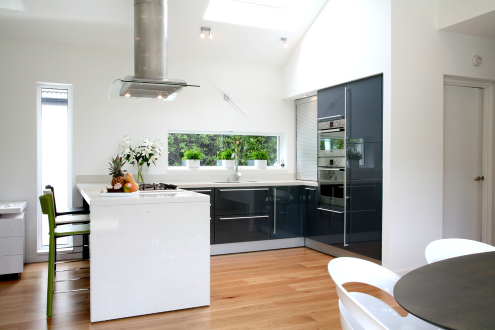 Photo of a mid-sized contemporary u-shaped eat-in kitchen in Dublin with flat-panel cabinets, grey cabinets, quartzite benchtops, white splashback, stainless steel appliances, light hardwood floors and with island.