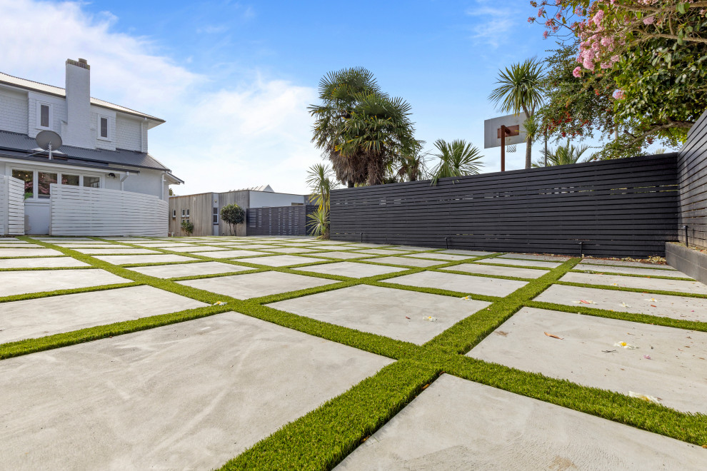 This is an example of a mid-sized modern front yard full sun driveway in Auckland with with lawn edging and concrete pavers.