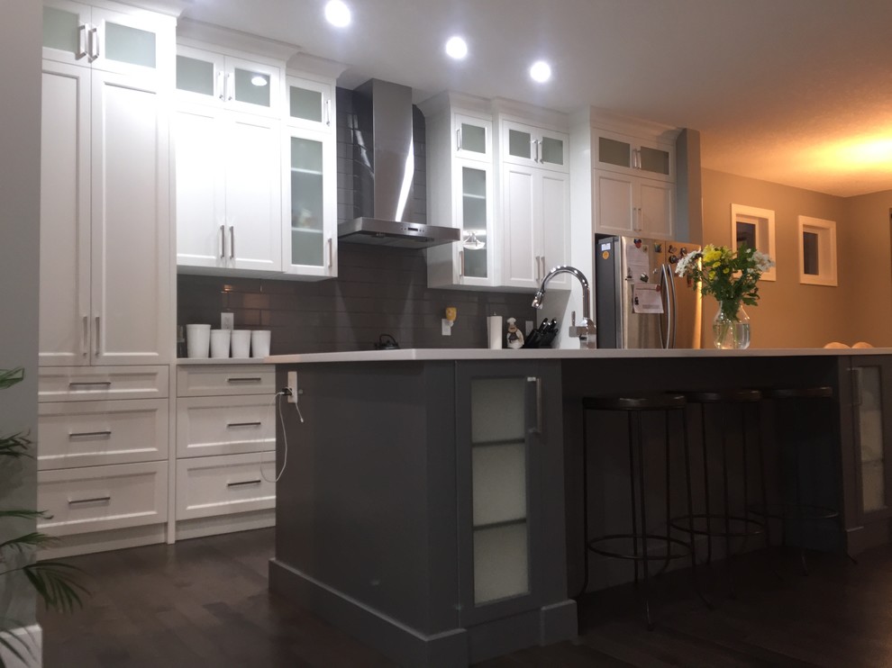 Mid-sized single-wall dark wood floor eat-in kitchen photo in Calgary with an undermount sink, shaker cabinets, white cabinets, quartzite countertops, gray backsplash, subway tile backsplash, stainless steel appliances and an island