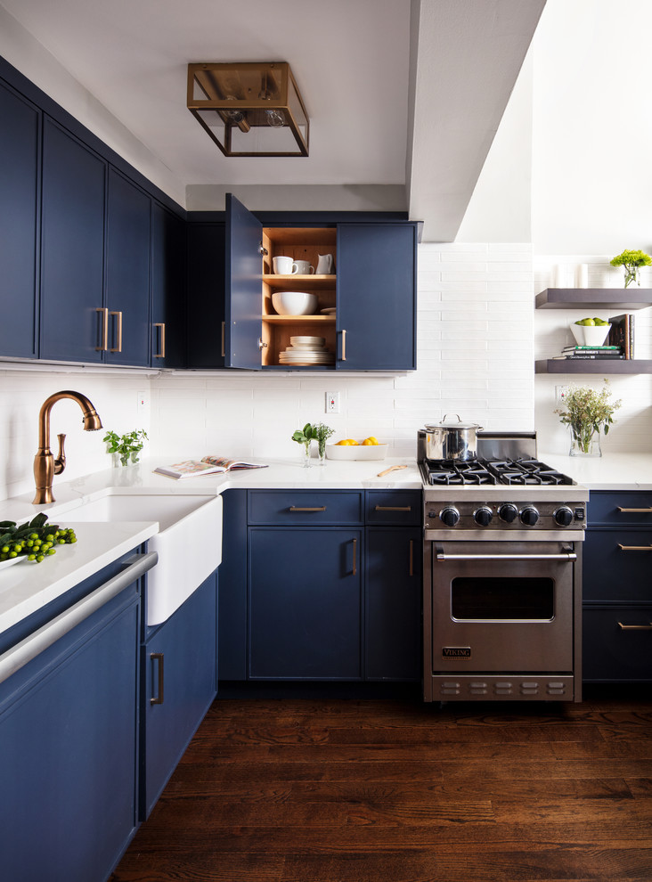 Small trendy dark wood floor and brown floor kitchen photo in New York with a farmhouse sink, blue cabinets, white backsplash, stainless steel appliances, white countertops, flat-panel cabinets, quartzite countertops, subway tile backsplash and no island