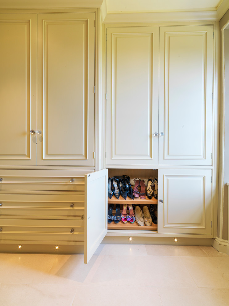 Large traditional gender-neutral built-in wardrobe in Other with raised-panel cabinets, limestone floors and yellow cabinets.