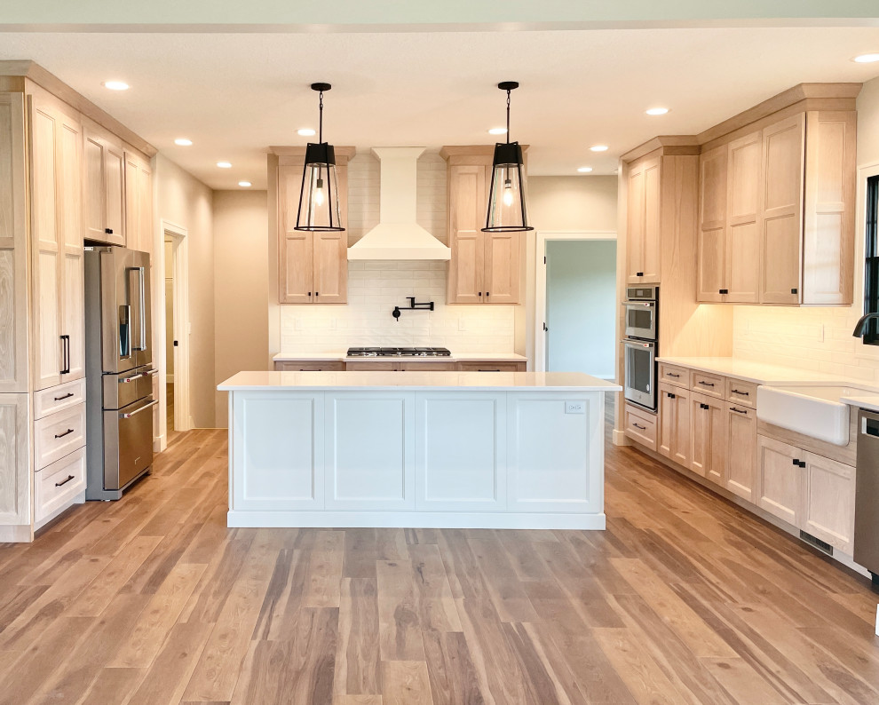 Photo of a large scandinavian u-shaped open plan kitchen in Other with a farmhouse sink, flat-panel cabinets, light wood cabinets, quartz benchtops, white splashback, porcelain splashback, stainless steel appliances, vinyl floors, with island, multi-coloured floor and white benchtop.