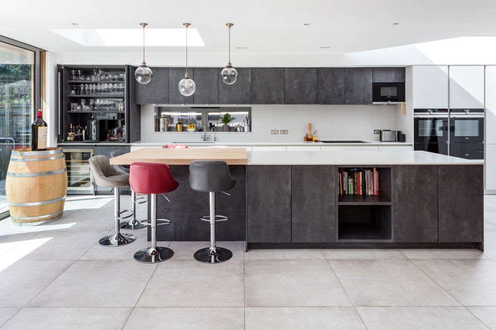 This is an example of a mid-sized contemporary galley open plan kitchen in London with a drop-in sink, flat-panel cabinets, grey cabinets, granite benchtops, white splashback, mirror splashback, panelled appliances, ceramic floors, with island, grey floor, white benchtop and recessed.