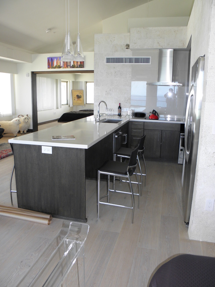 Design ideas for a mid-sized asian l-shaped eat-in kitchen in Hawaii with an undermount sink, flat-panel cabinets, black cabinets, solid surface benchtops, grey splashback, ceramic splashback, stainless steel appliances, light hardwood floors, a peninsula and grey floor.