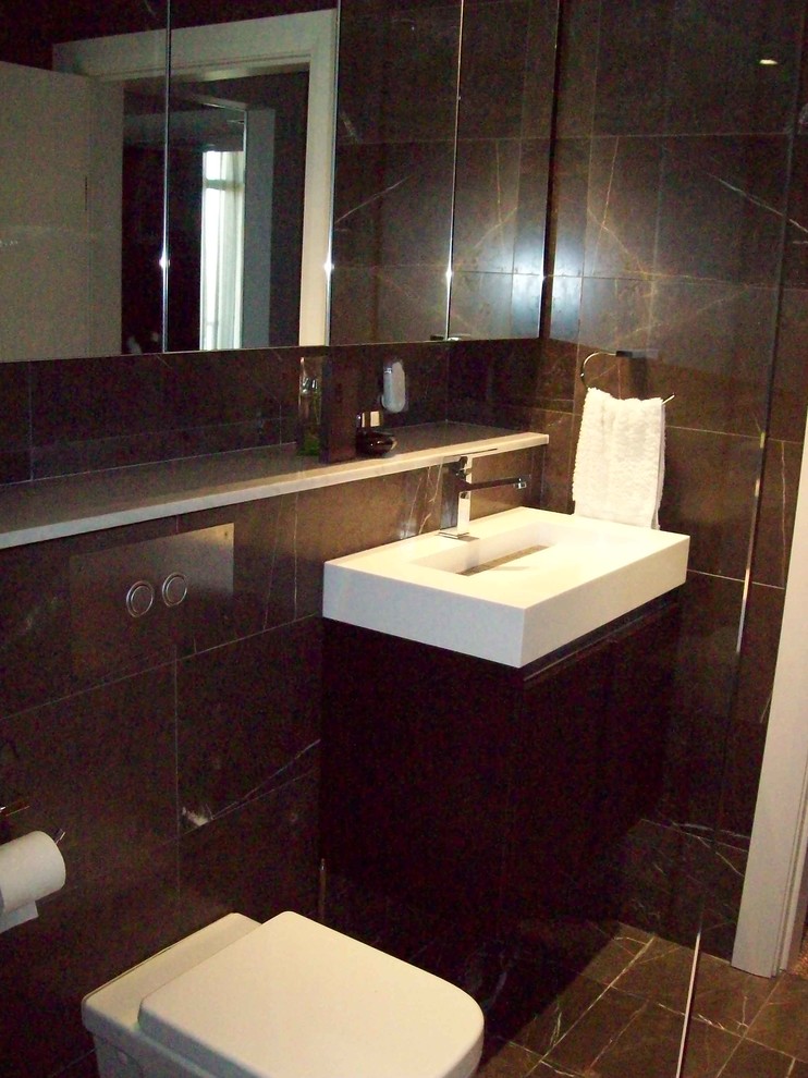 Photo of a mid-sized modern 3/4 bathroom in Sydney with an integrated sink, solid surface benchtops, a freestanding tub, a shower/bathtub combo, a wall-mount toilet, brown tile, porcelain tile, brown walls and porcelain floors.