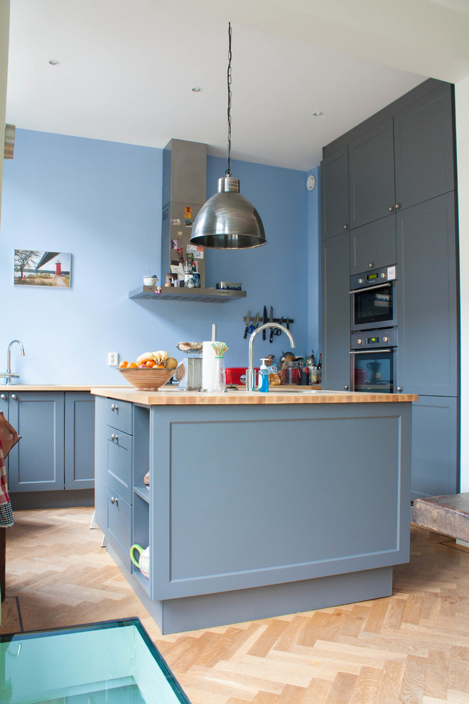Design ideas for an eclectic u-shaped kitchen in Amsterdam with blue cabinets, stainless steel appliances and medium hardwood floors.