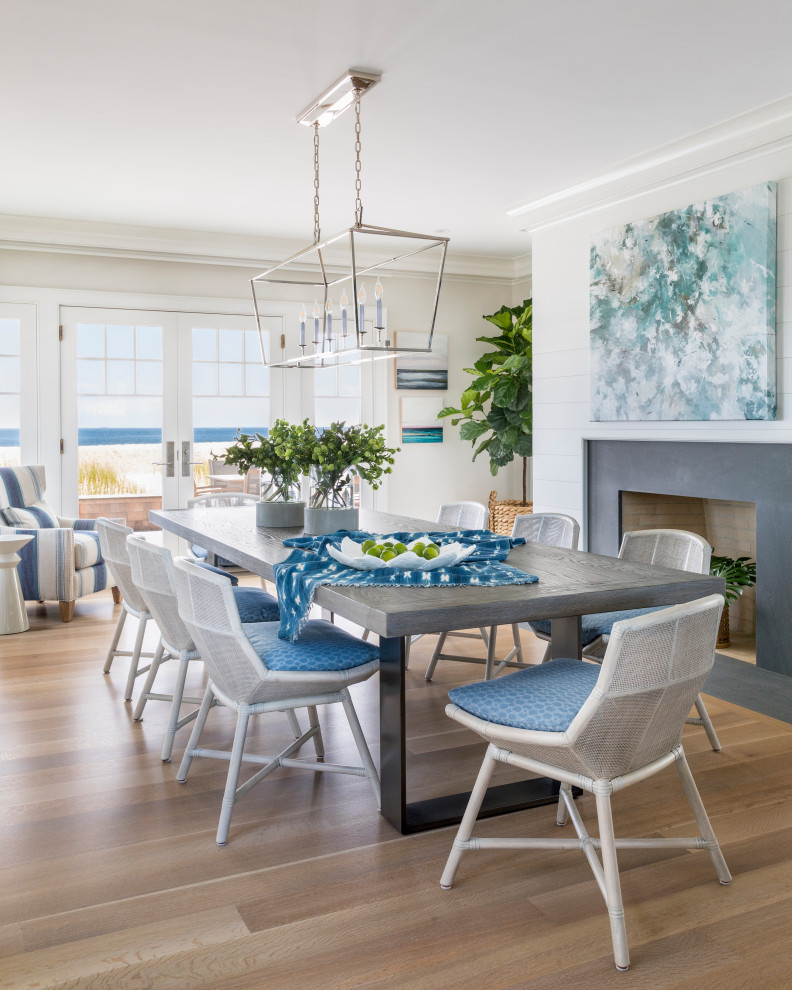 Design ideas for a beach style open plan dining in New York with white walls, light hardwood floors and a standard fireplace.