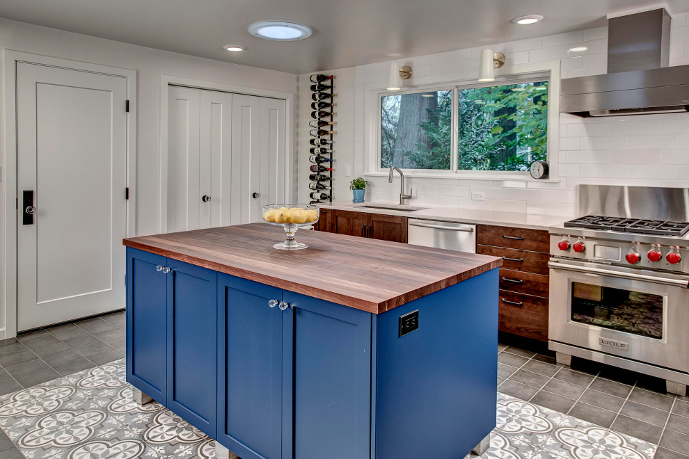 Design ideas for a mid-sized transitional eat-in kitchen in Seattle with a single-bowl sink, shaker cabinets, medium wood cabinets, wood benchtops, white splashback, porcelain splashback, stainless steel appliances, porcelain floors, with island, grey floor and brown benchtop.