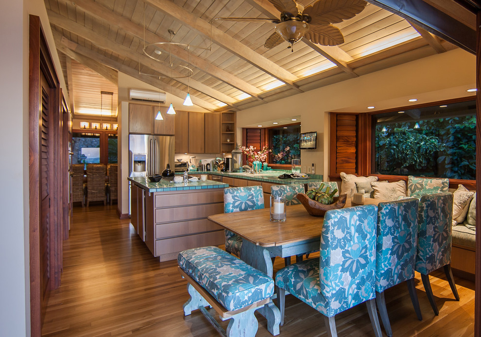 Photo of a mid-sized tropical l-shaped eat-in kitchen in Hawaii with flat-panel cabinets, medium wood cabinets, tile benchtops, stainless steel appliances, medium hardwood floors, with island, an undermount sink, green splashback, ceramic splashback and brown floor.