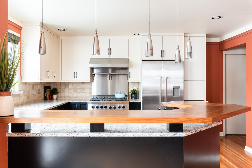 Inspiration for a mid-sized transitional u-shaped medium tone wood floor and brown floor eat-in kitchen remodel with an undermount sink, shaker cabinets, distressed cabinets, quartz countertops, white backsplash, travertine backsplash, stainless steel appliances, a peninsula and multicolored countertops