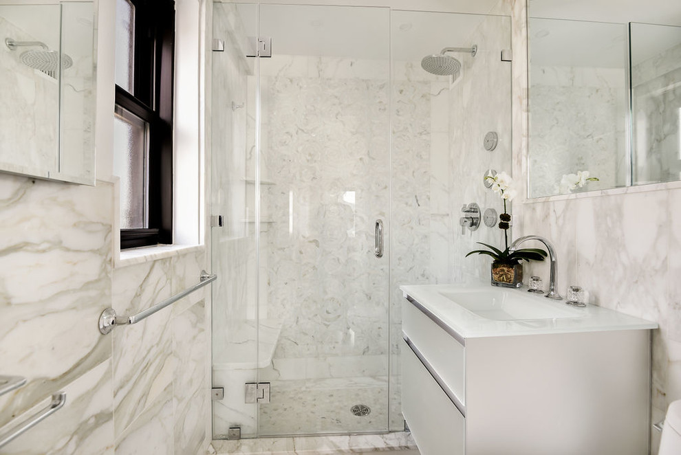 This is an example of a small transitional master bathroom in New York with glass-front cabinets, grey cabinets, an alcove shower, a one-piece toilet, gray tile, marble, grey walls, marble floors, an integrated sink, glass benchtops, grey floor and a hinged shower door.