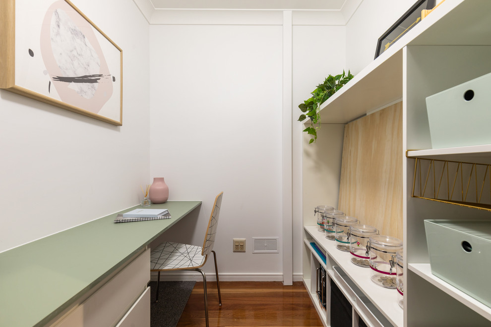 This is an example of a mid-sized transitional study room in Brisbane with white walls, medium hardwood floors, a built-in desk and brown floor.
