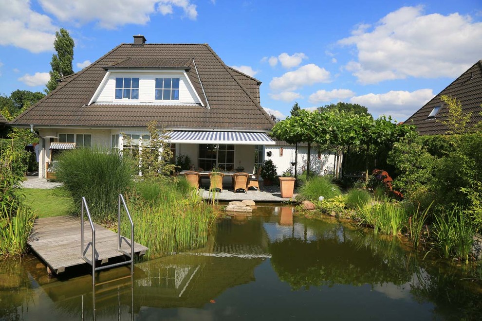 Large traditional backyard custom-shaped natural pool in Hamburg with decking.