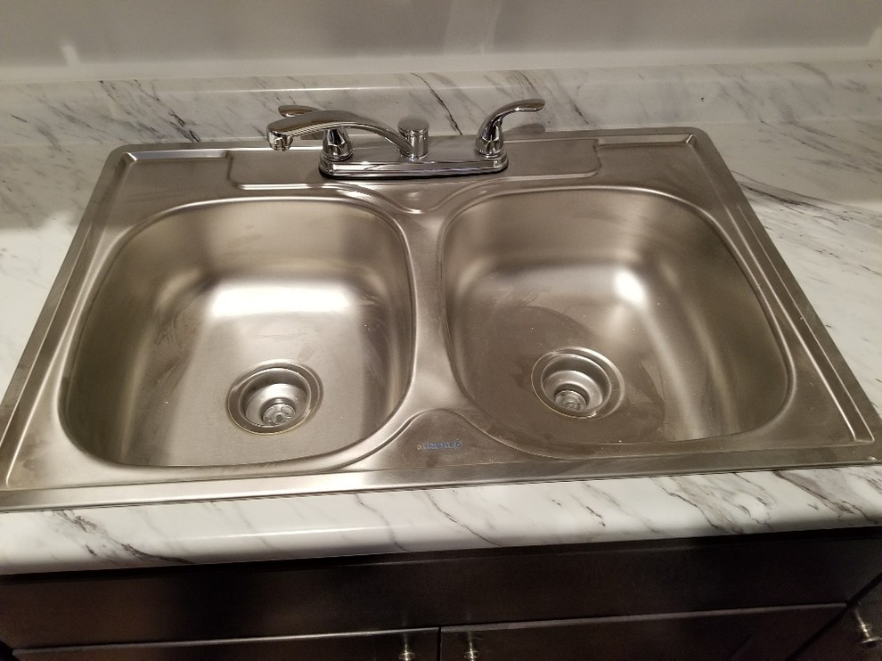 Example of a small transitional single-wall medium tone wood floor and brown floor kitchen design with a double-bowl sink, recessed-panel cabinets, dark wood cabinets, white backsplash, no island, white countertops and laminate countertops