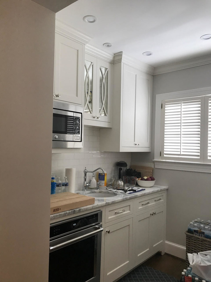 Enclosed kitchen - mid-sized transitional l-shaped brown floor and dark wood floor enclosed kitchen idea in DC Metro with an undermount sink, shaker cabinets, white cabinets, marble countertops, white backsplash, subway tile backsplash, paneled appliances and an island