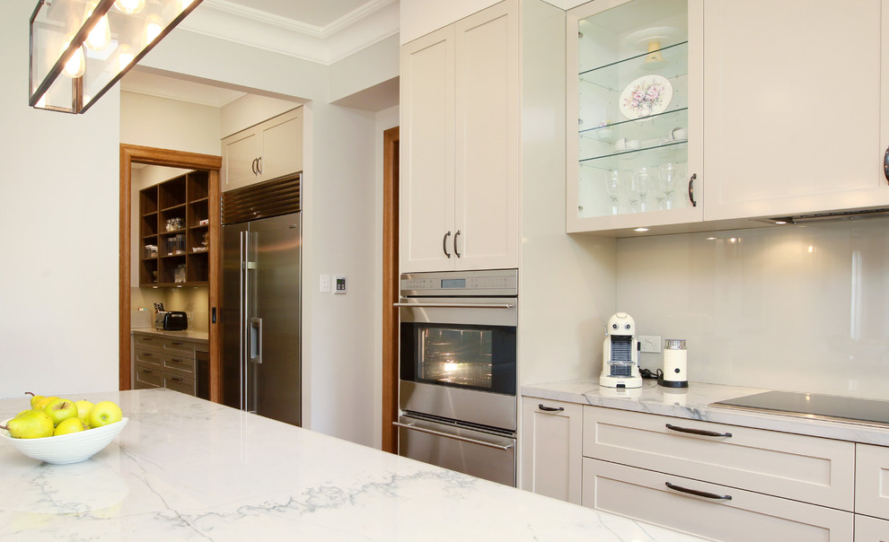 Photo of a large traditional galley eat-in kitchen in Melbourne with an undermount sink, shaker cabinets, beige cabinets, marble benchtops, beige splashback, glass sheet splashback, stainless steel appliances, medium hardwood floors and with island.