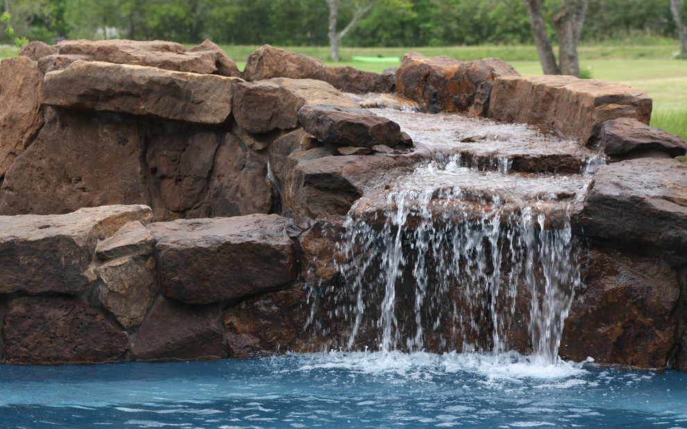 Photo of a large traditional backyard custom-shaped pool in Houston with a water feature and natural stone pavers.