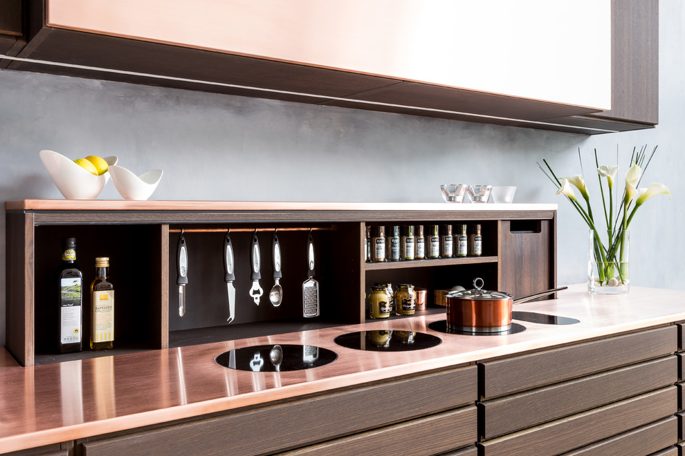 This is an example of a small contemporary single-wall open plan kitchen in London with a drop-in sink, flat-panel cabinets, brown cabinets, copper benchtops, grey splashback and no island.