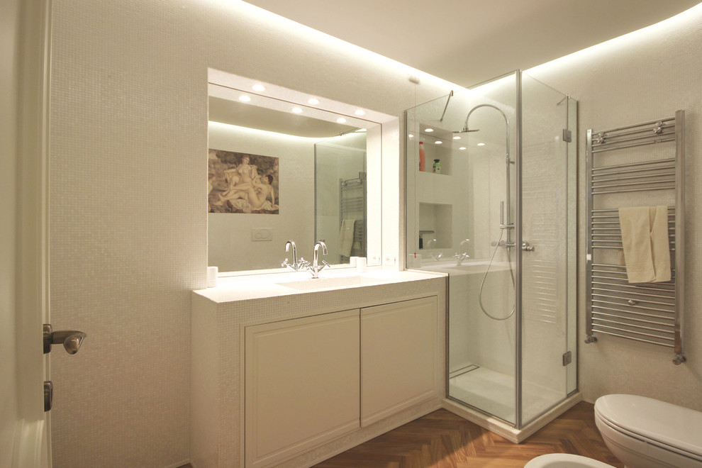 This is an example of a large traditional bathroom in Other with recessed-panel cabinets, white cabinets, a two-piece toilet, white tile, mosaic tile, white walls, medium hardwood floors, a drop-in sink, tile benchtops, brown floor and white benchtops.