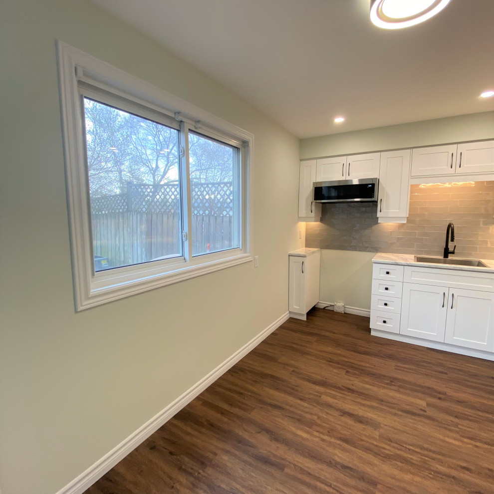 Mid-sized transitional galley vinyl floor eat-in kitchen photo in Toronto with a drop-in sink, shaker cabinets, white cabinets, laminate countertops, gray backsplash and stainless steel appliances