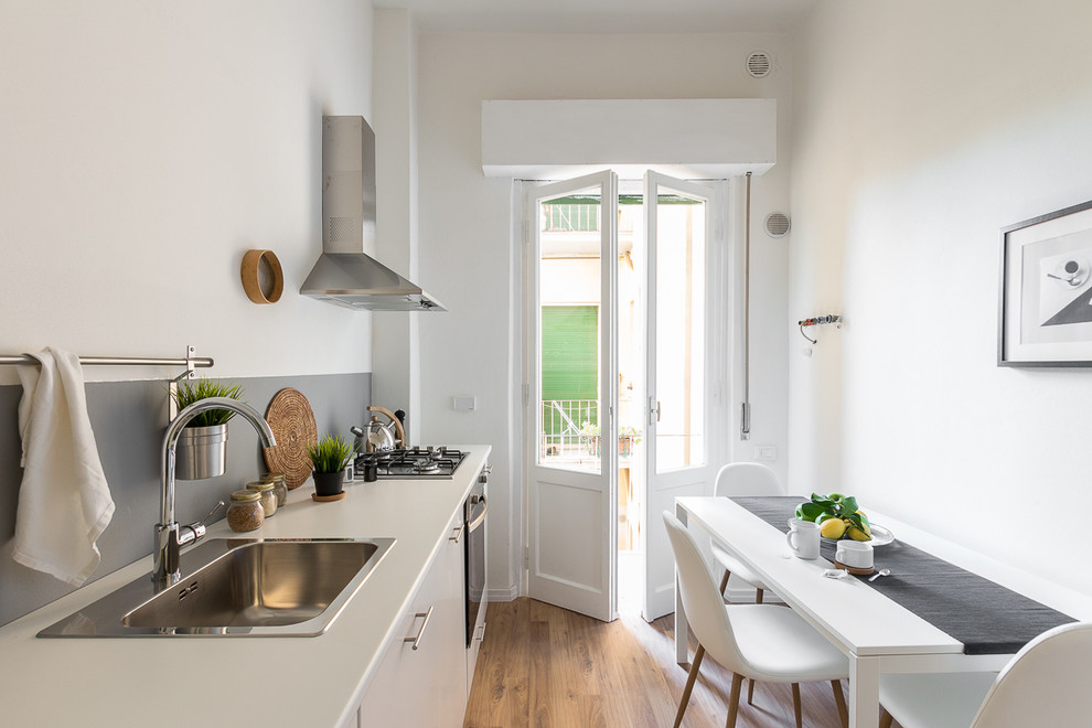 Small scandinavian single-wall eat-in kitchen in Florence with flat-panel cabinets, white cabinets, grey splashback, medium hardwood floors, no island, brown floor, a drop-in sink, glass sheet splashback and stainless steel appliances.
