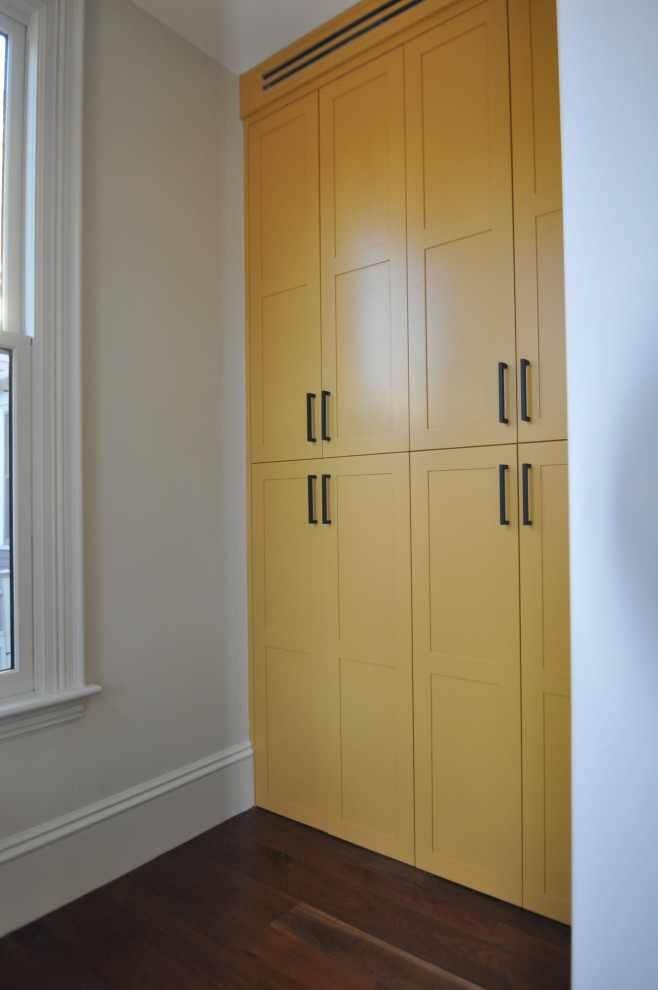 Réalisation d'une petite armoire encastrée tradition avec un placard avec porte à panneau encastré, des portes de placard jaunes, parquet foncé et un sol marron.
