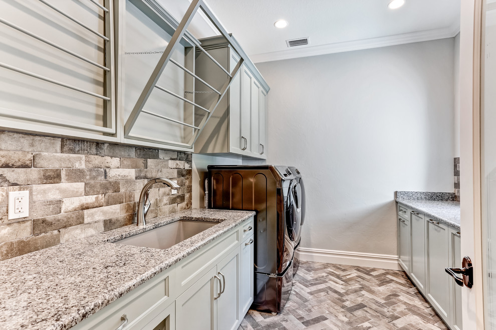 Design ideas for a mid-sized transitional galley laundry room in Tampa with an undermount sink, recessed-panel cabinets, grey cabinets, granite benchtops, grey walls, porcelain floors, a side-by-side washer and dryer, multi-coloured floor and multi-coloured benchtop.