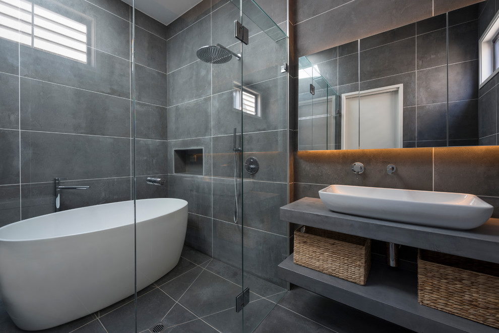 Photo of a contemporary master bathroom in Melbourne with open cabinets, grey cabinets, a japanese tub, an alcove shower, a one-piece toilet, gray tile, porcelain tile, grey walls, porcelain floors, a vessel sink and concrete benchtops.