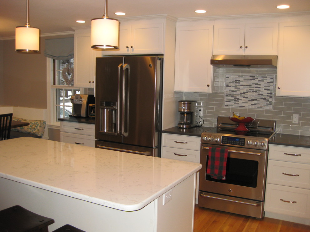 Transitional l-shaped medium tone wood floor eat-in kitchen photo in Boston with an undermount sink, white cabinets, quartz countertops, stainless steel appliances, an island, shaker cabinets, green backsplash, subway tile backsplash and black countertops