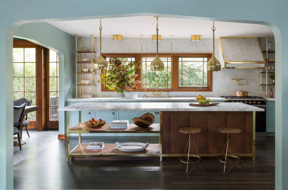Design ideas for a mid-sized transitional l-shaped eat-in kitchen in Portland with an undermount sink, blue cabinets, marble benchtops, white splashback, black appliances, dark hardwood floors, with island, brown floor, white benchtop, stone tile splashback and shaker cabinets.