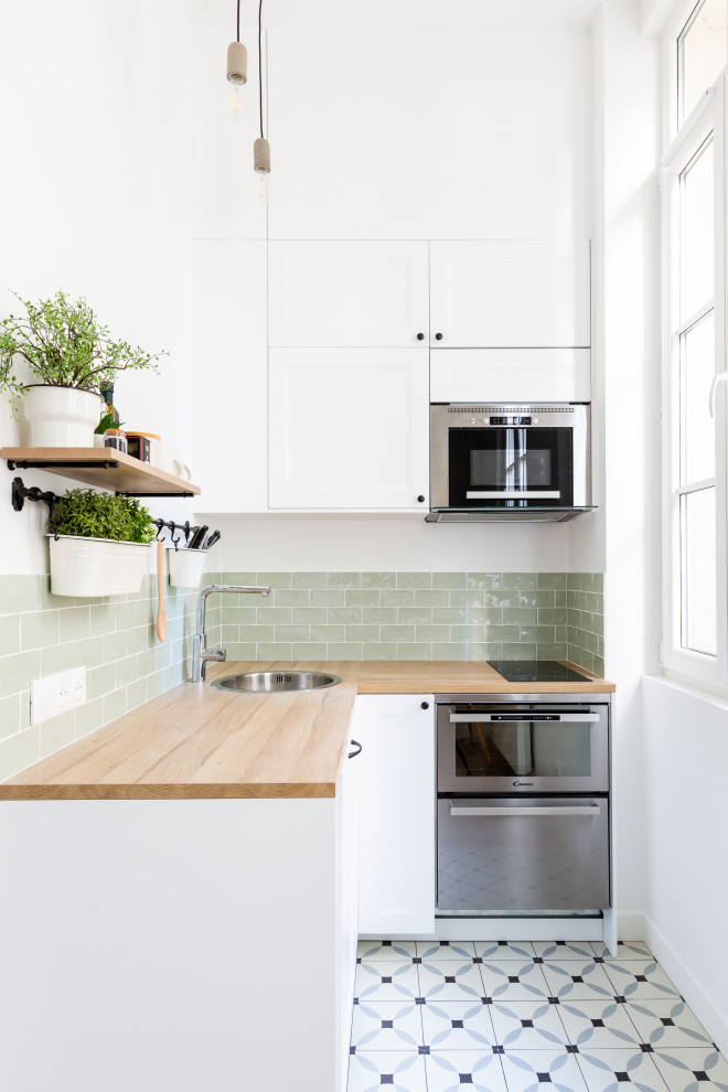 Inredning av ett skandinaviskt litet beige beige kök, med en undermonterad diskho, luckor med profilerade fronter, vita skåp, träbänkskiva, grönt stänkskydd, stänkskydd i keramik, rostfria vitvaror, cementgolv och flerfärgat golv