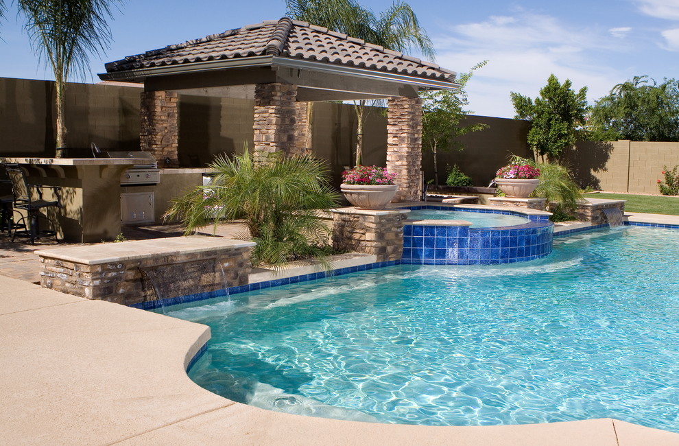 Photo of a large mediterranean backyard custom-shaped pool in Phoenix with a pool house and natural stone pavers.