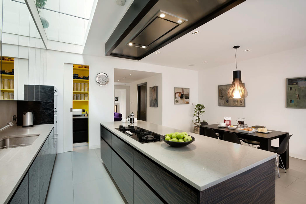 Large contemporary single-wall eat-in kitchen in London with a drop-in sink, flat-panel cabinets, dark wood cabinets, solid surface benchtops, grey splashback, stone slab splashback, stainless steel appliances, ceramic floors, with island, grey floor and grey benchtop.