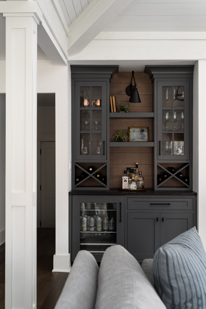 Photo of a country single-wall home bar in Chicago with no sink, glass-front cabinets, grey cabinets, brown splashback, timber splashback, dark hardwood floors, brown floor and black benchtop.