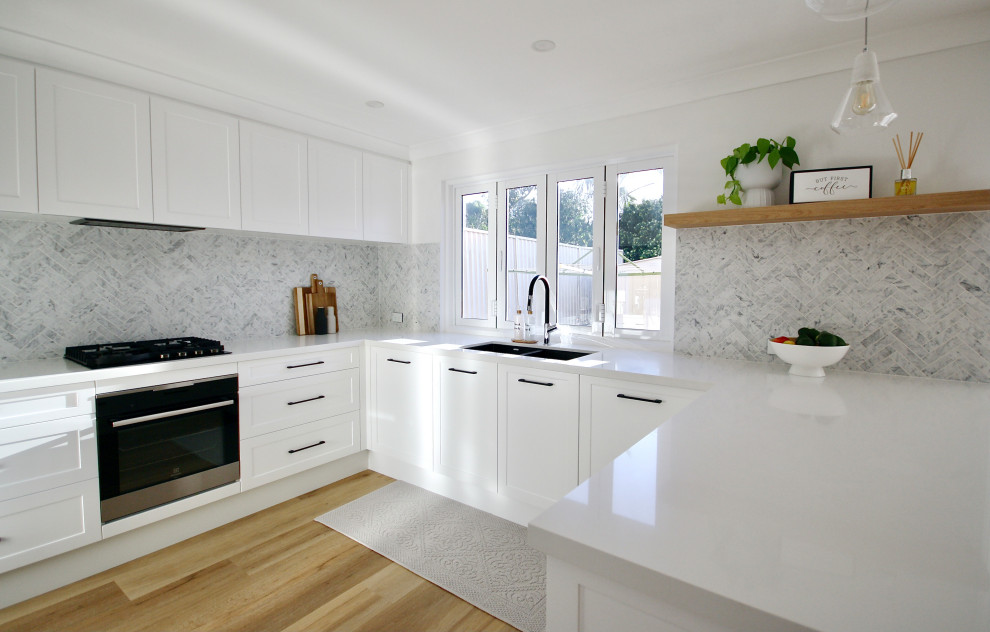 Idéer för ett mellanstort modernt vit kök, med en undermonterad diskho, skåp i shakerstil, vita skåp, bänkskiva i kvarts, grått stänkskydd, stänkskydd i marmor, svarta vitvaror, mellanmörkt trägolv, en köksö och brunt golv